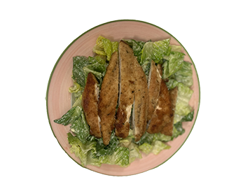 plate with green romaine lettuce and caesar dressing and topped with strips of breaded chicken cutlet